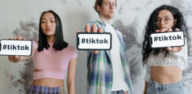 Two women and one man holding out their smartphones that display “#tiktok.”