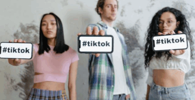 Two women and one man holding out their smartphones that display “#tiktok.”