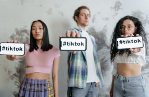 Two women and one man holding out their smartphones that display “#tiktok.”