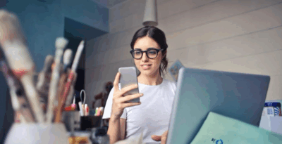 A woman looking at her phone while working on a laptop in a creative workspace