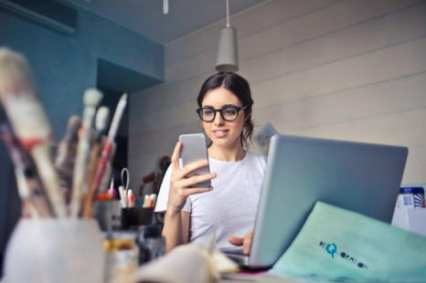 A woman looking at her phone while working on a laptop in a creative workspace